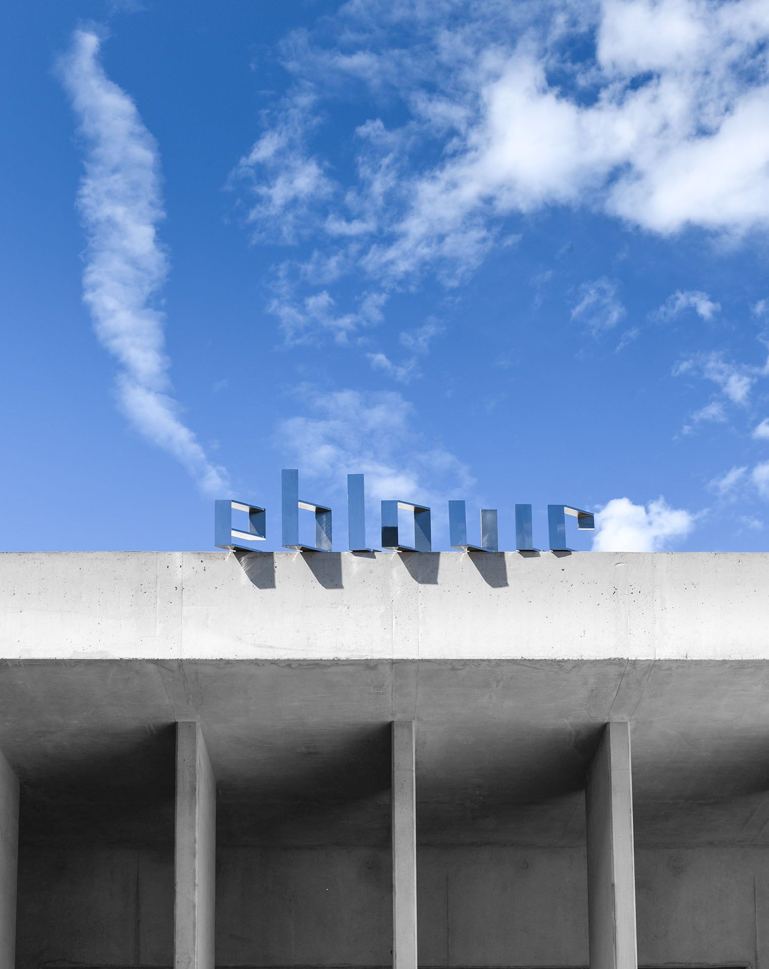 Lettres « éblouir » en contre-plongée sur le toit en béton sous ciel bleu.